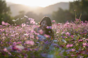 Young woman with floral crown smelling flowers in a vibrant field during sunset.