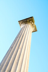 One tall antique marble column placed diagonally against the blue sky. Focus on the end of the column. Vertical photo