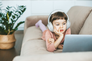 Reclining comfortably on a sofa, a cute 5-6-year-old girl watching a laptop screen, fully immersed in her digital world