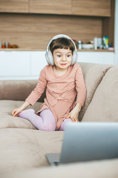 A girl with a funny grimace of surprise on her face watching a laptop, sitting on a sofa. Concept: technology-infused relaxation, online education, technological entertainment