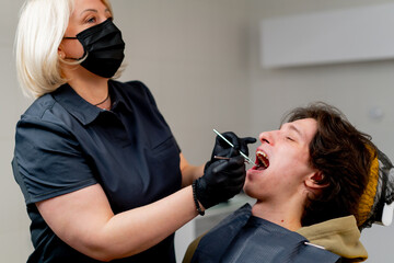 dental office doctor blonde dentist in black uniform consulting patient examining the mouth metal instruments