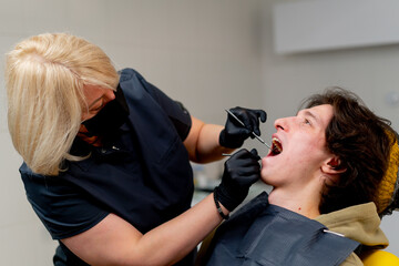 dental office doctor blonde dentist in black uniform consulting patient examining the mouth metal instruments