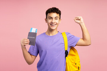 Attractive excited boy, teenager holding passport and boarding pass, backpack on shoulder, happy