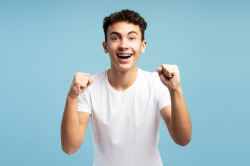 Fototapeta premium Happy excited fan boy with braces cheering, hands up, open mouth looking at camera