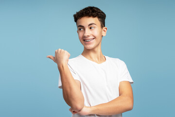 Smiling handsome teenage boy with braces showing finger on copy space looking away