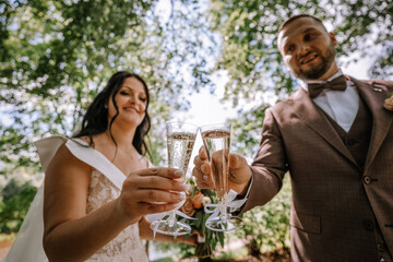 Valmiera, Latvia- July 28, 2024 - A bride and groom are toasting with champagne glasses, smiling on their wedding day in an outdoor setting.
