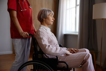 Aged senior woman in wheelchair having professional help at nursing home - 787133157
