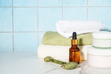 Skin care products in the bathroom. Face cream, serum bottle, jade roller and stack of towels. - 787144379