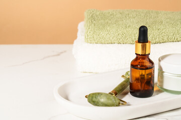 Face cream, serum bottle, jade roller and stack of towels in the bathroom. - 787144729