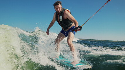 A man learns to wakesurf behind a boat. Fun on the water during the hot summer on the lake.