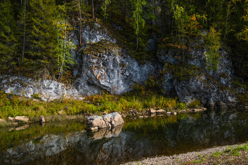 The river is near the rocks covered with forest .