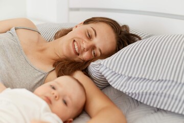 Obraz na płótnie Canvas Portrait Woman With Infant Baby Girl Boy Lying Bed Light Room Early Morning Enjoying Weekend Spending Time Together Happy Parenthood