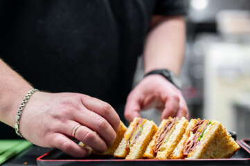 Freshly prepared sandwich, neatly sliced to reveal layers of ingredients, held in a tray by a...