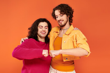 cheerful young gay friends in stylish vivid outfits posing together on orange backdrop, pride