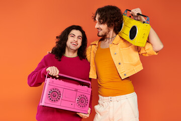 two cheerful attractive gay friends in vibrant clothes posing with tape recorders, pride month