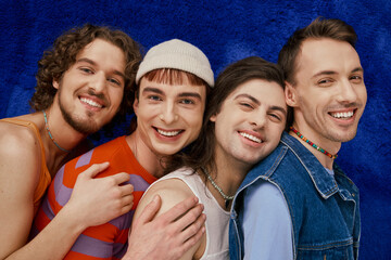 four joyful appealing stylish gay friends in everyday bright attires on blue backdrop, pride month
