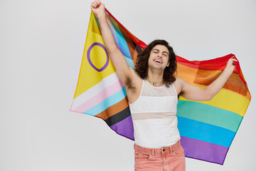 appealing joyous gay man with long dark hair posing with rainbow flag and looking at camera