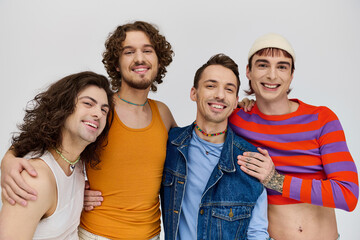 four jolly good looking gay men in vivid attires smiling at camera while posing on gray backdrop