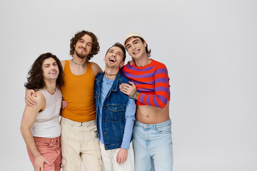 four delighted attractive gay men in vivid attires smiling at camera while posing on gray backdrop