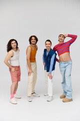 Fototapeta premium four joyous good looking gay men in vivid attires smiling at camera while posing on gray backdrop