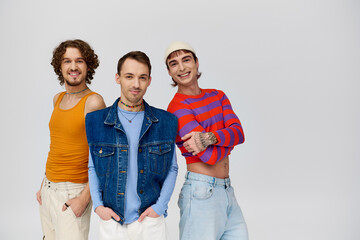 joyous handsome gay men in vibrant attires posing together on gray backdrop and looking at camera