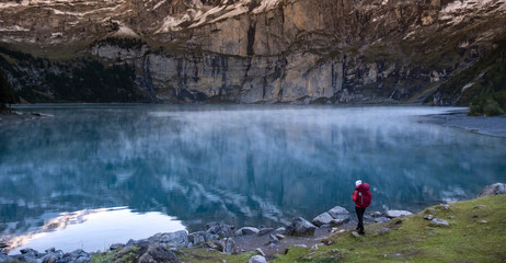 Sporty girl looking into reflection of mountains in lake. Lake Oeschinensee in Swiss alps. Travel,...