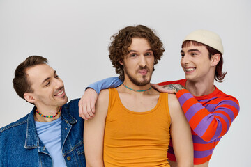Fototapeta premium positive young gay men in vibrant attires posing together on gray backdrop and looking at camera