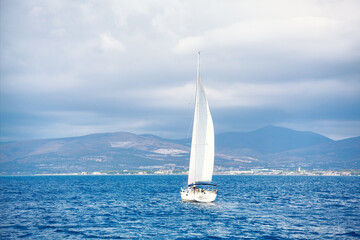 Luxury white yacht sails across the azure open sea. Large mast with white sails