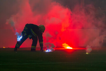 Fireman picking up burning torches during a football match.  Football fans' torches fire on the field