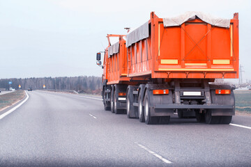 Fototapeta na wymiar An orange grain dump truck with a semi-trailer transports grain along the road from a farm. Transportation of grain harvest. Copy space for text, agricultural