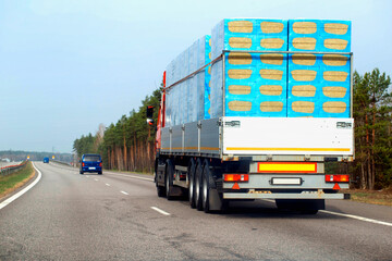 A truck with a semi-trailer transports a bulk load of insulation for construction along a country road in the spring. Copy space for text, industry