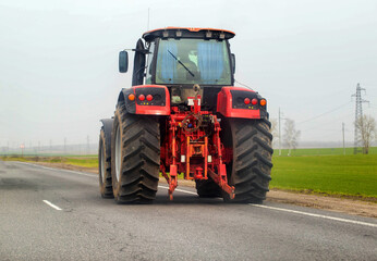 A modern red tractor drives on the highway against the background of fields. Concept of agricultural machinery on country roads. Copy space for text, industry