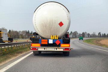 A tanker semi-trailer truck transports a dangerous cargo of gasoline, diesel fuel and petroleum products on the road against the backdrop of the sun. Cargo hazard class. Copy space for text