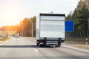A modern van with a tail lift is driving along an asphalt road against the backdrop of a sunset....