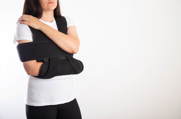 A girl in a black medical brace on the shoulder joint for rehabilitation after a fracture of the humerus and dislocation. Post-traumatic immobilization of the shoulder joint  - 787161538