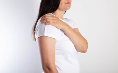 A girl on a white background is holding her shoulder and has aching pain. The concept of bursitis and pain of the shoulder joint. Brachial neuritis and brachial plexitis, glenohumeral periatritis