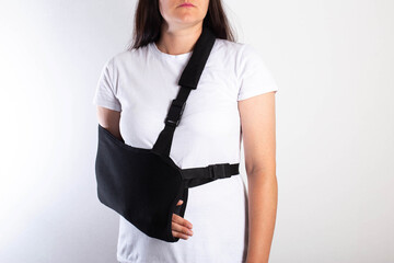 A girl on a white background with a black supporting medical bandage after a dislocation of the shoulder joint and a bone fracture. Rehabilitation after injury, orthopedics and traumatology