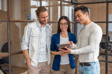 Three young business professionals standing together and discussing over business report in office hallway. Office colleagues checking a business document on the tablet in coworking