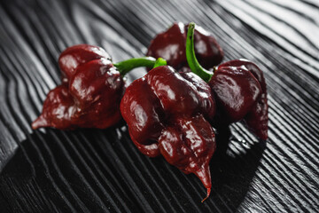 fresh brown extra hot carolina reaper chocolate pepper on black wooden rustic background