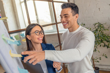 Creative people working on new project. Smiling asian woman looking at her colleague whom telling about some job details. Startup development and problem solving together