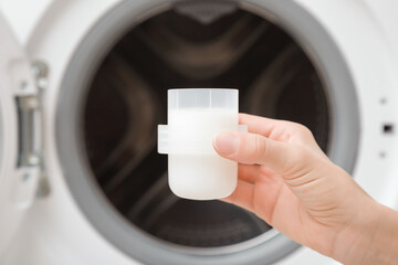 Young adult woman hand holding plastic bottle cap of white softener for clothes washing. Closeup. Front view.