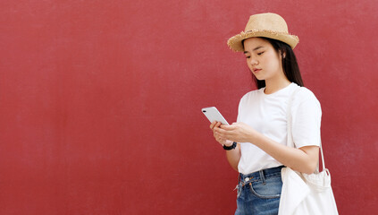 Young asian woman using phone with smiling, happy and relax emotion, over red background with copy space, Happy asia girl on phone, people and technology, lifestyle