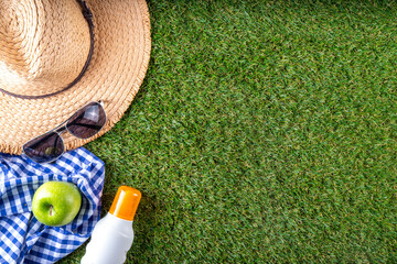 Spring, summer picnic, outdoor recreation background. A woman's straw hat, a picnic blanket or tablecloth, sunscreen spray, an apple on a background of green artificial grass or lawn, copy space - 787167115
