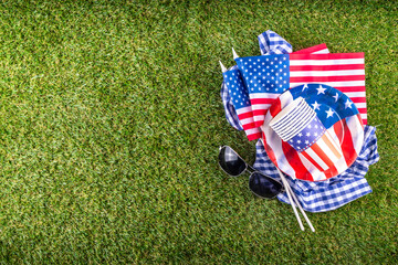 July 4, Independence Day traditional American picnic background. Plates, glasses, USA flags on green lawn or meadow grass, with blanket or tablecloth for picnic, sunglasses, copy space top view - 787167169