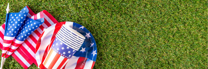 July 4, Independence Day traditional American picnic background. Plates, glasses, USA flags on green lawn or meadow grass, with blanket or tablecloth for picnic, sunglasses, copy space top view - 787167337