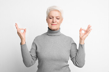 Serene senior lady with meditative pose on grey background