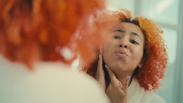 African American woman upset with face skin imperfections, looking in the mirror