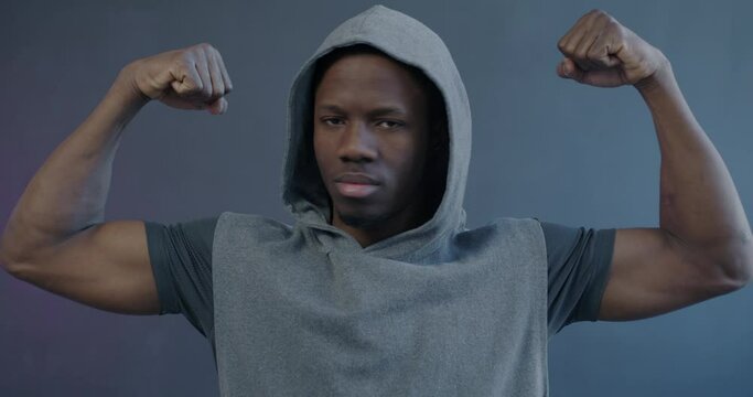 Slow motion portrait of strong young African American man showing biceps muscles and looking at camera on purple background. Bodybuilding and macho concept.