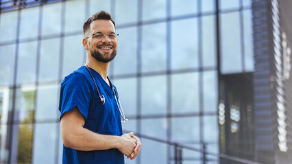 Portrait of male nurse at hospital. Portrait of a smiling doctor. Doctor with stethoscope standing, crossed arms, isolated on bright background. Portrait of a friendly doctor smiling at the camera. - obrazy, fototapety, plakaty