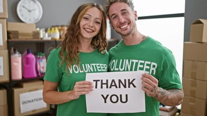 Two volunteers, a man and a woman, holding a 'thank you' sign in a donation center warehouse.